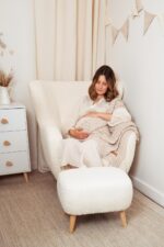 Pregnant woman resting in an armchair with the Fema bamboo baby blanket in warm beige