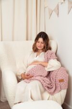 Pregnant woman in an armchair with the Fema bamboo baby blanket in misty rose