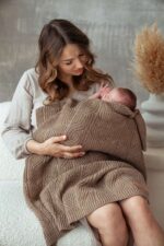 Mother holding a baby wrapped in the Bono merino blanket in warm brown