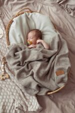 Baby with a dummy in a wicker basket under the all-season Meri merino blanket in beige