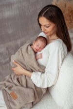 Mother holding a newborn wrapped in the all-season Meri merino blanket in beige
