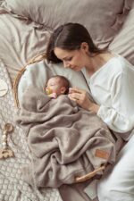 Mother lying beside a baby in a wicker basket under the all-season Meri merino blanket in beige