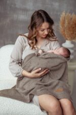 Mother holding a sleeping newborn wrapped in the all-season Meri merino blanket in dark beige