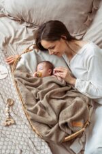 Newborn with a dummy in a wicker basket under the all-season Meri merino blanket in warm brown, mother beside