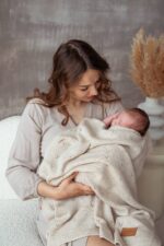 Mother holding a sleeping newborn in the all-season Meri merino blanket in warm beige