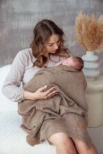 Mother holding a newborn wrapped in the all-season Meri merino blanket in warm brown