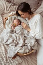 Birdsong bamboo muslin swaddle covering a baby in a wicker basket next to the mother