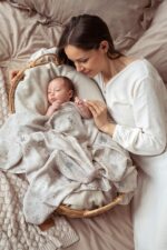 Mother touching the hand of a baby covered with the Birdsong bamboo muslin swaddle
