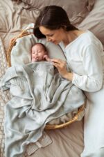 Mother with a baby covered with the Happy Goose Olive bamboo muslin swaddle in a basket