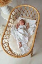 Baby in a rattan bassinet with the Happy Goose bamboo swaddle and Happy Goose pillow