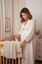 Pregnant woman placing the Fema bamboo baby blanket in warm beige over a cot