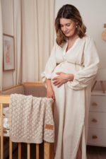 Pregnant woman in a nursery with the Fema bamboo blanket in warm beige hung on a cot