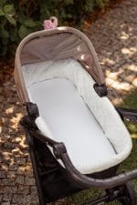 White pram sheet fitted on the mattress of a pram in a garden