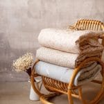 Folded filled duvets, including the sage Happy Goose Olive, stacked on a rattan chair