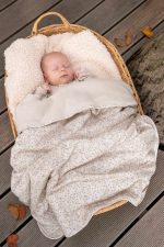 Sleeping baby in a wicker basket under the warm Herbs cotton blanket with a tiny sprig print