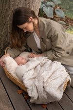 Mother leaning over a baby in a basket covered with the Herbs cotton blanket