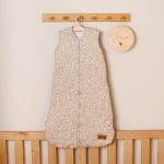Beige Herbs baby sleeping bag with tiny sprigs on a hanger above a cot