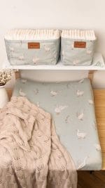 Changing pad in the Happy Goose Olive cover under an openwork blanket, with baskets above