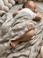 Śpiące niemowlę przykryte beżowym kocykiem bambusowym Ivi o ażurowym wzorze liści