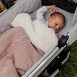 Newborn in a pram under the Bruno sherpa-lined blanket in pastel pink