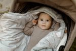 Baby in a pram in the unzipped Happy Goose Olive footmuff with a goose print