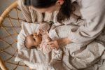 Mama otula niemowlę leżące na poduszce Herbs w rattanowym koszu