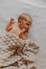 Newborn on a bed covered to the waist with the Fema bamboo blanket in warm beige