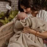 Mama tuli niemowlę owinięte kocykiem bambusowym Bibi w kolorze cappuccino, siedząc w ogrodzie