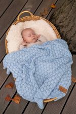 Niemowlę śpi w wiklinowym koszu na tarasie pod kocykiem bambusowym Fema w kolorze baby blue