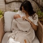 Mother in a garden chair cuddling a baby wrapped in the Fema bamboo blanket in beige