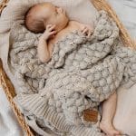 Newborn in a wicker basket covered with the Fema bamboo blanket in beige