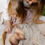 Mother and big sister leaning over a baby under the beige Fema bamboo blanket