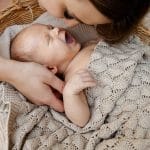 Yawning baby in a basket covered with the Fema bamboo blanket in beige, mother beside