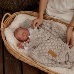 Mother tucking a newborn in a wicker basket under the beige Fema bamboo blanket
