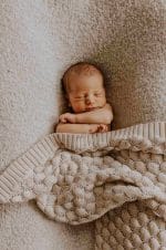 Sleeping newborn covered up to the shoulders with the Fema bamboo blanket in warm beige