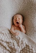 Yawning newborn under the Fema bamboo blanket in warm beige