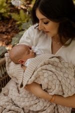 Mother in a garden holding a baby wrapped in the Fema bamboo blanket in warm beige
