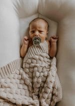 Newborn with a pacifier in a baby nest covered with the Fema bamboo blanket in warm beige