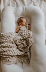 Newborn in a white baby nest covered with the Fema bamboo blanket in warm beige
