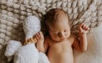 Sleeping newborn with a soft toy on the Fema bamboo blanket in warm beige