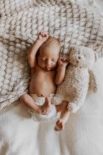 Stretching newborn with a teddy bear on the Fema bamboo blanket in warm beige