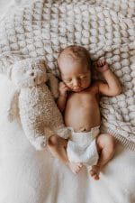 Newborn with a teddy bear lying on the spread Fema bamboo blanket in warm beige