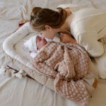 Mother kissing a baby lying in the Happy Goose baby nest under a pink bamboo blanket