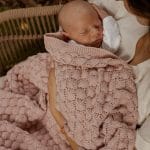 Sleeping newborn in his mother's arms wrapped in the Fema bamboo blanket in misty rose