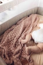 Baby in a cot with its feet on the Fema bamboo blanket in misty rose