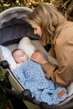 Mama przykrywa niemowlę w wózku kocykiem bambusowym Fema w kolorze baby blue