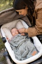 Mother tending to a baby in a pram bassinet covered with the olive Hana bamboo blanket