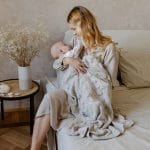 Mama na łóżku tuli niemowlę okryte beżowym ażurowym kocykiem bambusowym Ivi