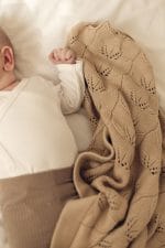 Rączka niemowlęcia trzymająca ażurowy kocyk bambusowy Ivi w kolorze cappuccino