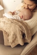 Mama całuje niemowlę w główkę, na kolanach kocyk bambusowy Ivi w kolorze cappuccino